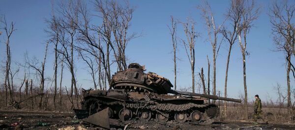 A fighter with the separatist self-proclaimed Donetsk People's Republic army looks at a destroyed Ukrainian army tank near the town of Debaltseve February 22, 2015 - Sputnik Mundo