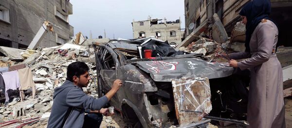 Palestinian artists paint on the remains of car that witnesses said was destroyed by Israeli shelling during a 50-day war - Sputnik Mundo