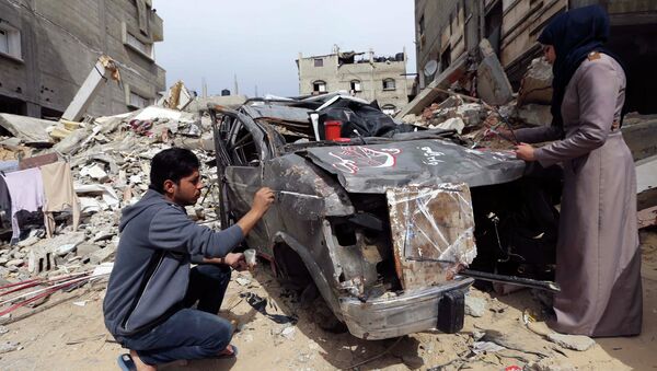 Palestinian artists paint on the remains of car that witnesses said was destroyed by Israeli shelling during a 50-day war - Sputnik Mundo