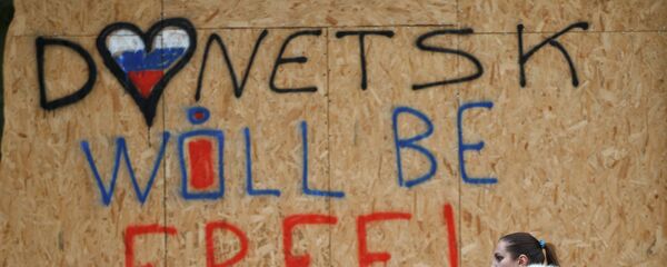 Una mujer camina frente a un local protegido ante posibles bombardeos con tablas de madera, en las que se lee Donetsk será libre - Sputnik Mundo