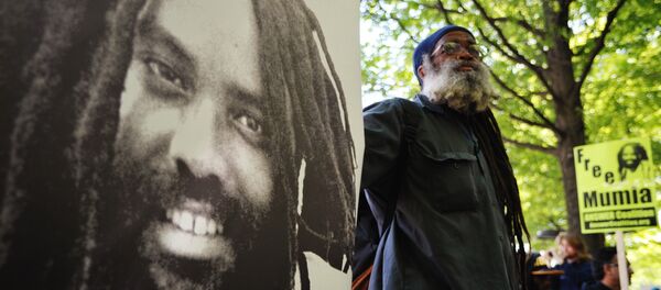 A protestor stands next to an image of Mumia Abu-Jamal outside the US Department of Justice on April 24, 2012 - Sputnik Mundo