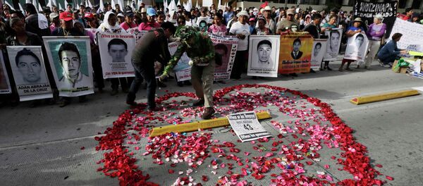 A man spreads rose petals in the shape of a heart as relatives hold up posters of some of the 43 missing students of the Ayotzinapa Teacher Training College A man spreads rose petals in the shape of a heart as relatives hold up posters of some of the 43 missing students of the Ayotzinapa Teacher Training College - Sputnik Mundo