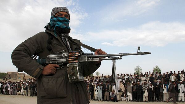 A member of the Taliban insurgent and other people stand at the site during the execution of three men in Ghazni Province on April 18, 2015. - Sputnik Mundo