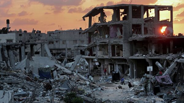 Palestinians walk during the sunset between the rubble of their destroyed building in Shijaiyah neighborhood of Gaza City in the northern Gaza Strip, Sunday, Oct. 12, 2014 - Sputnik Mundo