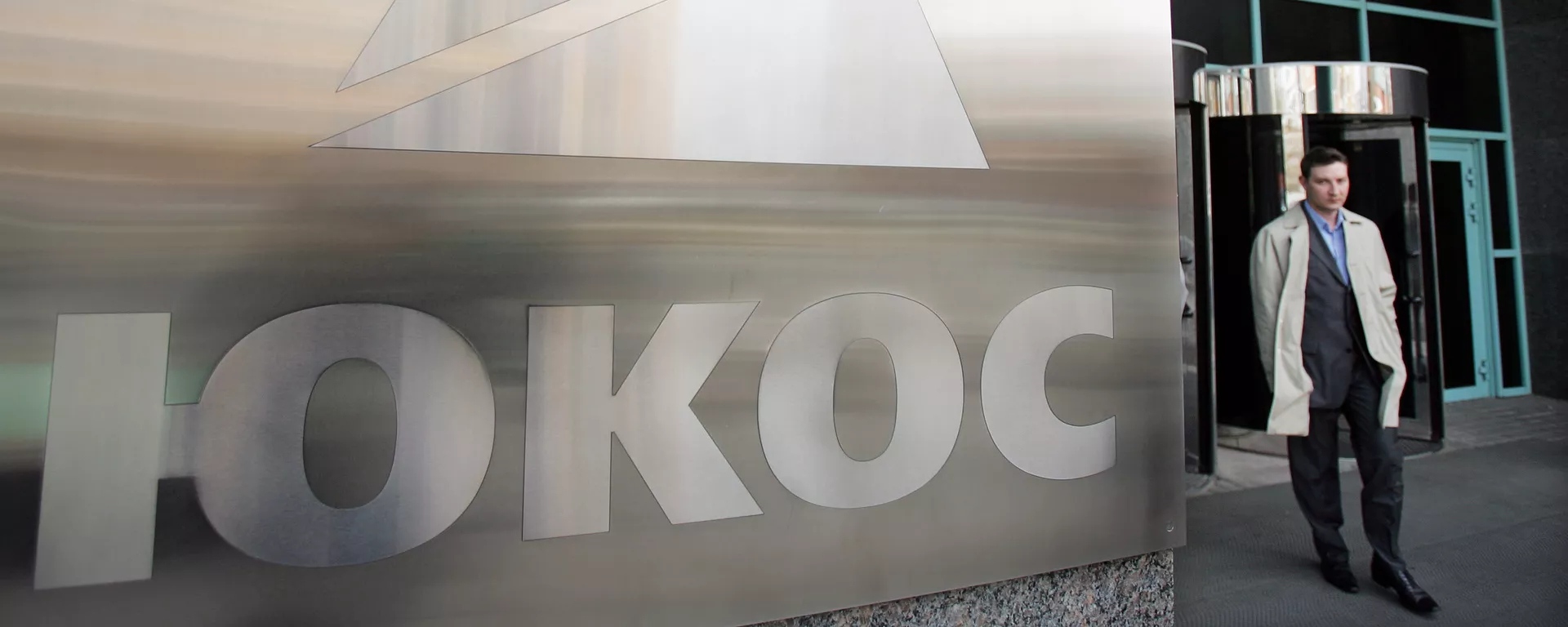 A man passes by a Yukos logo at the headquarters of the oil company in Moscow after the latest auction for the sale of package of assets the stricken giant, 04 April 2007 A man passes by a Yukos logo at the headquarters of the oil company in Moscow after the latest auction for the sale of package of assets the stricken giant, 04 April 2007 - Sputnik Mundo, 1920, 29.07.2021