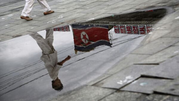 A North Korean woman is reflected in a rain puddle as she walks past the country's national flag along the Kim Il Sung Square on Sunday, July 21, 2013, downtown Pyongyang, North Korea - Sputnik Mundo