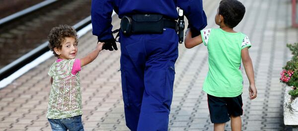 A police officer escorts migrant children along a platform to a waiting train bound for Munich, at the railway station in Hegyeshalom, Hungary - Sputnik Mundo