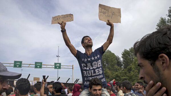 A migrant holds a banner reading Germany help as he sits on another migrant's shoulders in front of a barrier at the border with Hungary near the village of Horgos, Serbia - Sputnik Mundo