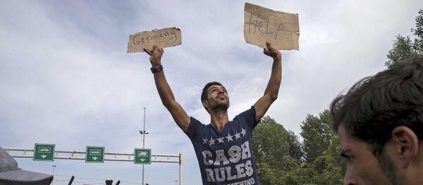 A migrant holds a banner reading Germany help as he sits on another migrant's shoulders in front of a barrier at the border with Hungary near the village of Horgos, Serbia - Sputnik Mundo