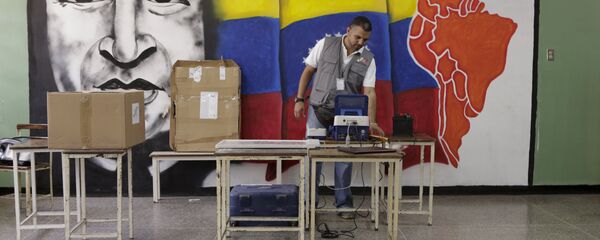 A worker of the National Electoral Council (CNE) configures a voting machine in front of a mural depicting Venezuela's late President Hugo Chavez at a school in Caracas, December 4, 2015. Venezuela will hold parliamentary elections on December 6. - Sputnik Mundo
