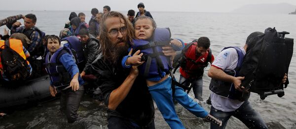 Un voluntario lleva a una pequeña refugiada siria tras un naufragio cerca de las costas de Turquía - Sputnik Mundo