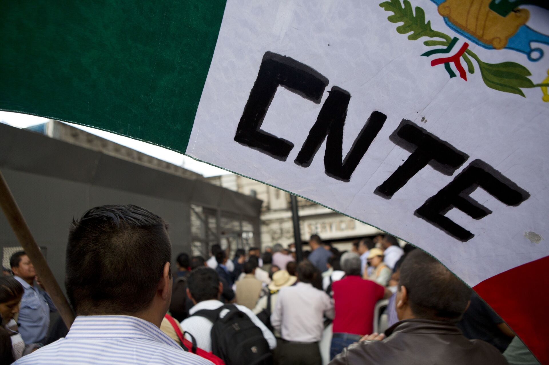 A protesting teacher holds a flag from the CNTE teachers union, as a group of teachers and a mediation commission, pass through a security barrier outside the Interior Ministry - Sputnik Mundo, 1920, 24.04.2026