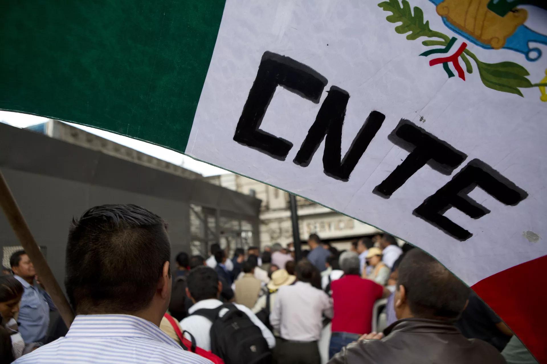 A protesting teacher holds a flag from the CNTE teachers union, as a group of teachers and a mediation commission, pass through a security barrier outside the Interior Ministry - Sputnik Mundo, 1920, 24.04.2026