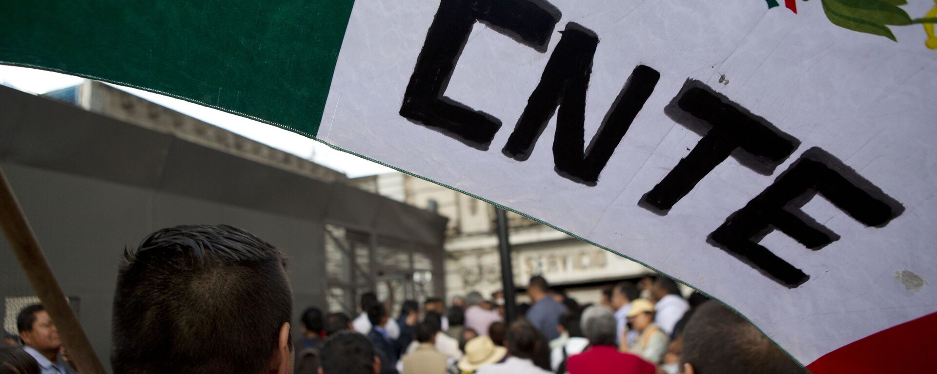 A protesting teacher holds a flag from the CNTE teachers union, as a group of teachers and a mediation commission, pass through a security barrier outside the Interior Ministry - Sputnik Mundo, 1920, 09.06.2026