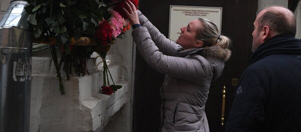 Una mujer deposita flores frente a la sede de la fundación benéfica Ayuda Justa - Sputnik Mundo