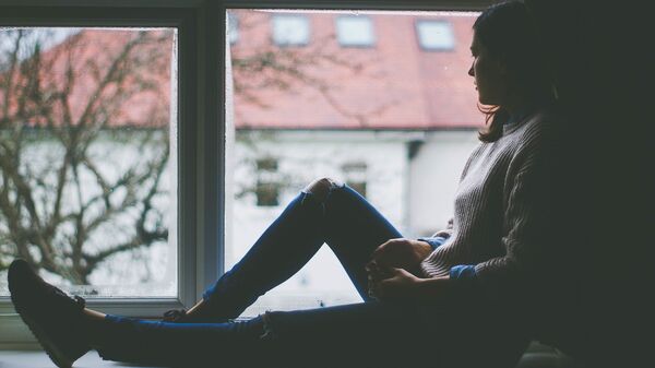 Una mujer pensativa mira por la ventana (imagen referencial) - Sputnik Mundo