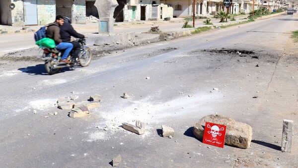 Men ride a motorbike past a hazard sign at a site hit by an airstrike on Tuesday in the town of Khan Sheikhoun in rebel-held Idlib - Sputnik Mundo