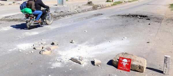 Men ride a motorbike past a hazard sign at a site hit by an airstrike on Tuesday in the town of Khan Sheikhoun in rebel-held Idlib - Sputnik Mundo