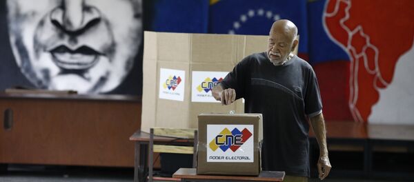Un venezolano está votando en las elecciones presidenciales en Caracas con una imagen del expresidente del país, Hugo Chávez, de fondo - Sputnik Mundo