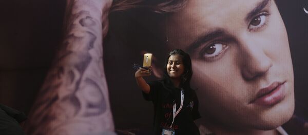 Una fan del cantante canadiense Justin Bieber se hace un selfi delante de una fotografía del astro - Sputnik Mundo