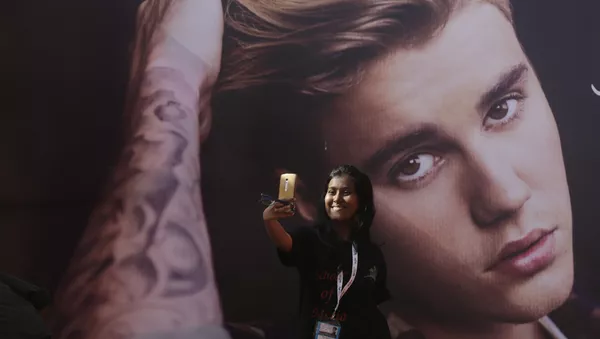 Una fan del cantante canadiense Justin Bieber se hace un selfi delante de una fotografía del astro - Sputnik Mundo