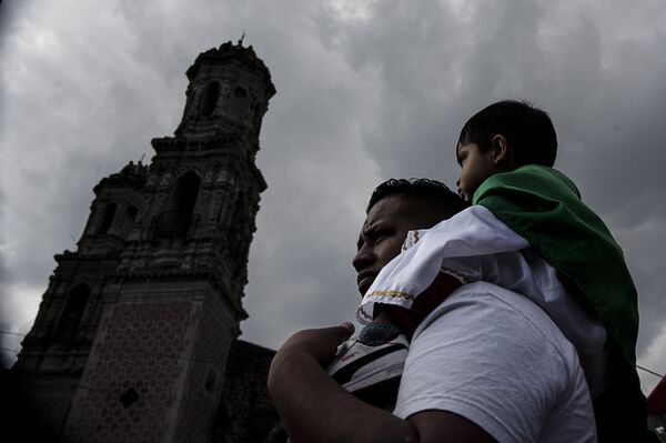 Padre carga a su hijo vestido como San Judas Tadeo frente al Templo de San Hipólito, en la Ciudad de México - Sputnik Mundo
