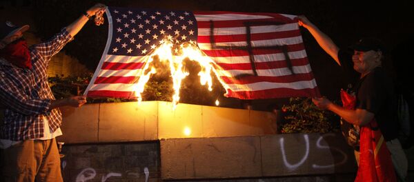 Dos personas están quemando una bandera de Estados Unidos durante una protesta a favor de la caravana de migrantes frente a la embajada estadounidense en Tegucigalpa, Honduras Dos personas están quemando una bandera de Estados Unidos durante una protesta a favor de la caravana de migrantes frente a la embajada estadounidense en Tegucigalpa, Honduras - Sputnik Mundo