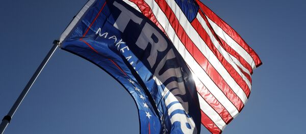 Un partidario del candidato presidencial republicano Donald Trump sostiene la bandera estadounidense y una bandera de campaña de Trump - Sputnik Mundo