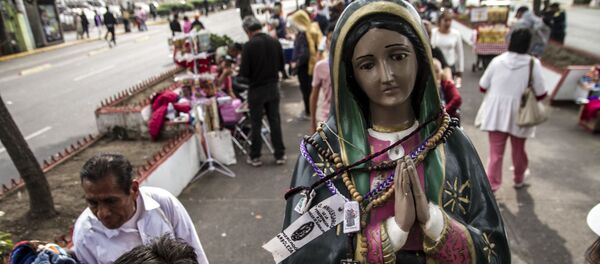 Mujer camina con una estatua de la Virgen de Guadalupe - Sputnik Mundo