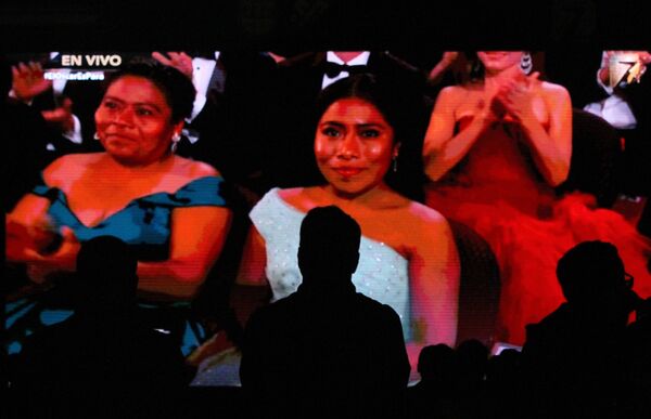 Un hombre en la proyección de los premios Oscar, de fondo ve a Yalitza Aparicio junto a su madre en la premiación de los Oscar 2019.  - Sputnik Mundo