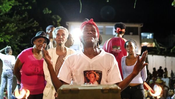 Una mujer reza frente a la estatuilla de San Juan durante la celebración del Día de San Juan Bautista en Curiepe. - Sputnik Mundo
