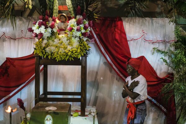 Una mujer reza a un costado de la estatuilla de San Juan durante la celebración del Día de San Juan Bautista en Curiepe. - Sputnik Mundo