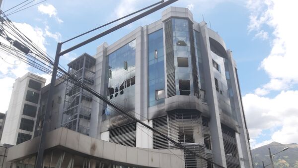 El edificio de la Contraloría General de Ecuador, en Quito, luego de que grupos de encapuchados, lo atacaron y prendieron fuego a varias de sus oficinas. Los vidrios rotos, el olor a humo, el color negruzco de sus paredes, son los vestigios del último fin de semana, en que la violencia se apoderó de Quito, en medio de las protestas por el incremento de los precios de los combustibles. - Sputnik Mundo