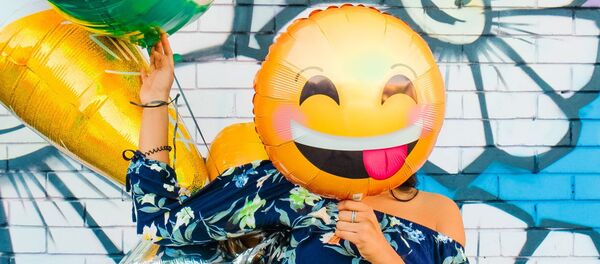 Una persona sostiene un balón de emoji sobre su rostro - Sputnik Mundo