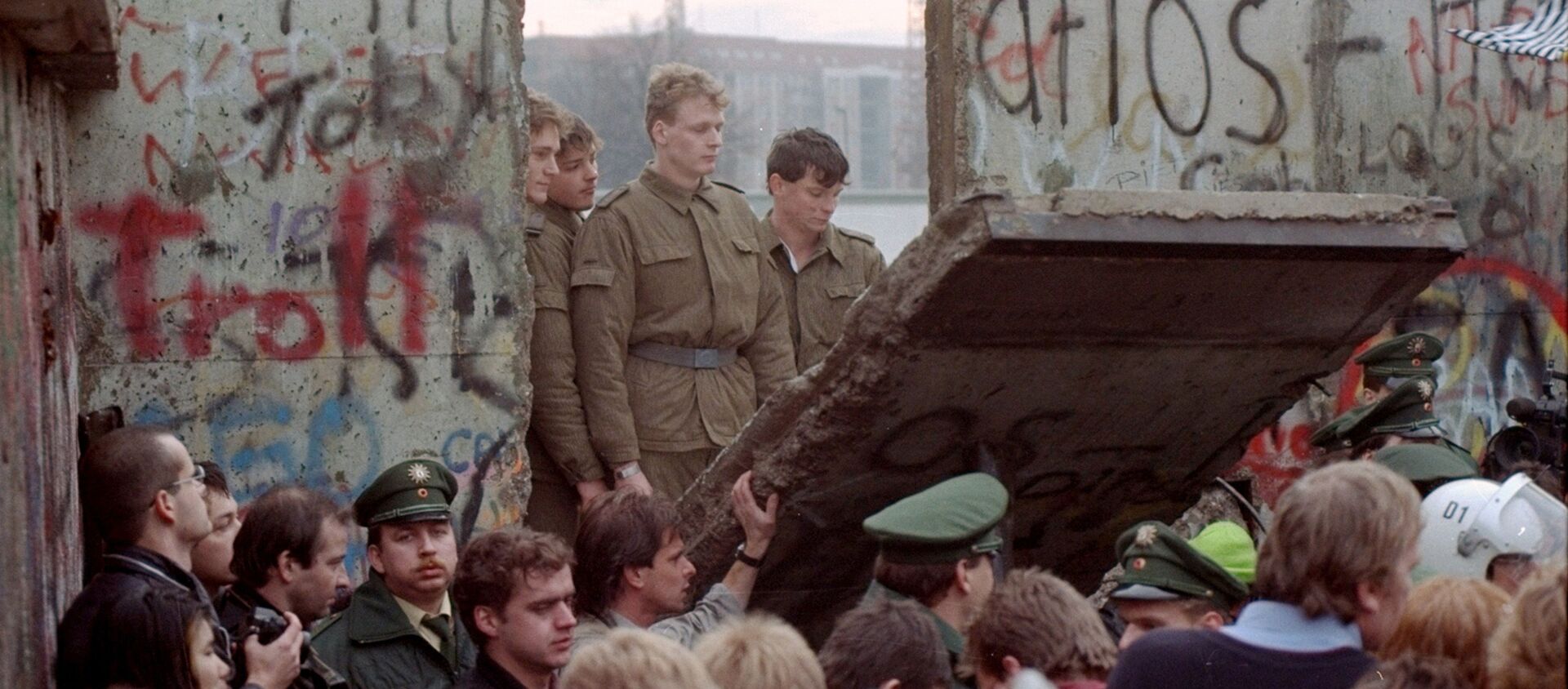 Guardias fronterizos de Alemania Oriental aparecen tras el muro de Berlín después que los manifestantes derribaron un segmento Guardias fronterizos de Alemania Oriental aparecen tras el muro de Berlín después que los manifestantes derribaron un segmento - Sputnik Mundo, 1920, 08.11.2019