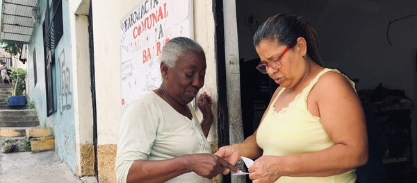 Manuela, dueña de la casa donde está la farmacia comunal, entregando unos medicamentos a una vecina del barrio Manuela, dueña de la casa donde está la farmacia comunal, entregando unos medicamentos a una vecina del barrio - Sputnik Mundo