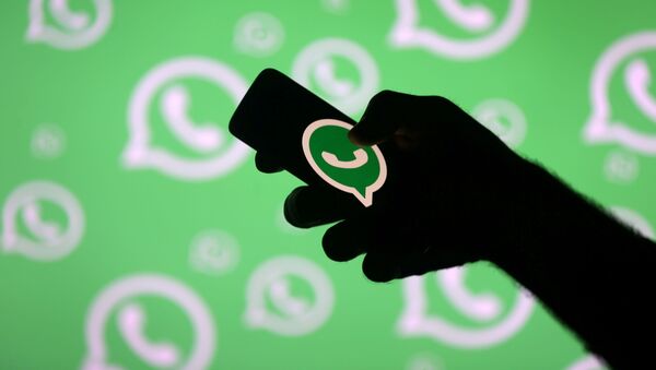 Una persona posa con un teléfono inteligente delante de una pared con el logotipo de WhatsApp  - Sputnik Mundo