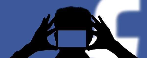 Una persona con un teléfono móvil con el logo de Facebook de fondo - Sputnik Mundo