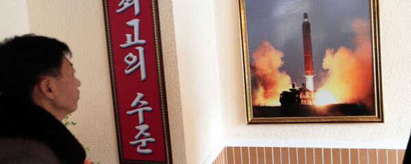 Un hombre mira la foto del lanzamiento de un misil norcoreano - Sputnik Mundo