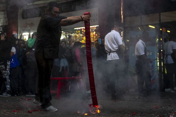 Uno de los locatarios prende una tira de cohetes frente a su negocio durante los festejos del Año Nuevo chino en la Ciudad de México. Los cohetes y música alejan los malos pensamientos y espíritus del lugar. - Sputnik Mundo