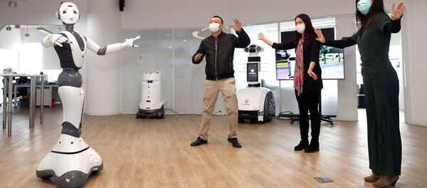 Los miembros del personal que llevan máscarillas gesticulan junto a un robot 5G con el fin de dar consejos médicos relacionados con coronavirus - Sputnik Mundo