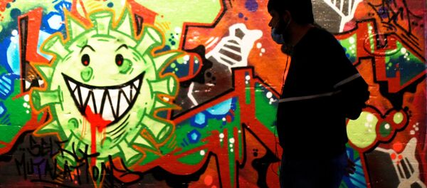 Un hombre con una mascarilla pasa al lado de un muro con un grafiti del coronavirus en el centro de Londres - Sputnik Mundo