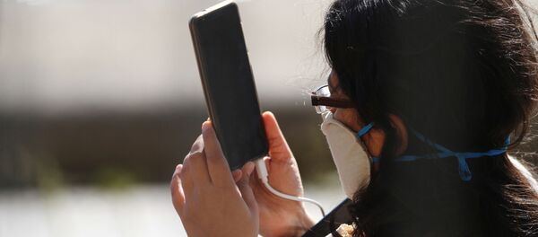 Una persona con una mascarilla utiliza su móvil - Sputnik Mundo