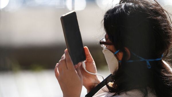 Una persona con una mascarilla utiliza su móvil - Sputnik Mundo