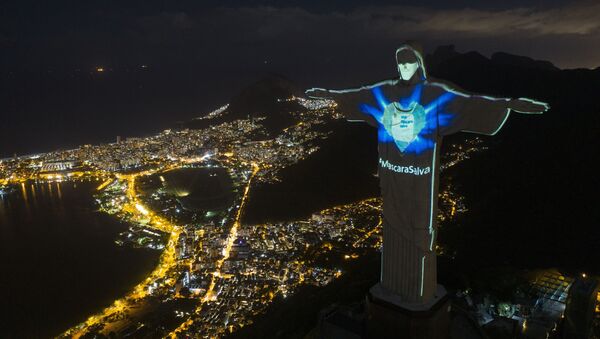 Estatua de Cristo Redentor con iluminación en forma de máscara y con una inscripción en portugués que reza 'La máscara salva' en Río de Janeiro, Brasil. - Sputnik Mundo