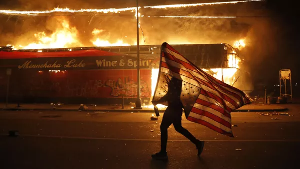 Un manifestante alza la bandera de EEUU al revés en las protestas en Minneapolis. El asesinato de George Floyd, un afroamericano de 46 años, a manos de la policía ha causado una espiral de disturbios en la ciudad. El vídeo donde se observa cómo Floyd pide no ser asfixiado ha dado la vuelta al mundo y ha evidenciado la violencia policial que sufre la comunidad afrodescendiente en el país norteamericano.  - Sputnik Mundo