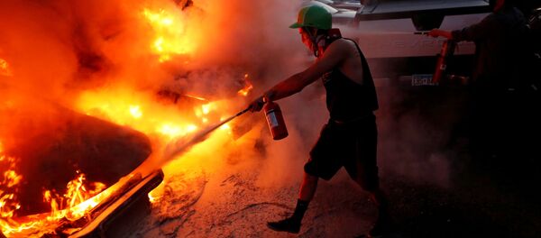 Un hombre trata de apagar el fuego en un vehículo durante una protesta en Minneapolis por la muerte de George Floyd - Sputnik Mundo