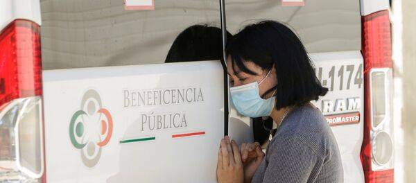 Mujer con mascarilla junta a ambulancia - Sputnik Mundo