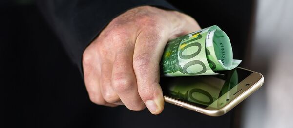 Una persona sostiene un movil y algunos billetes Una persona sostiene un movil y algunos billetes - Sputnik Mundo