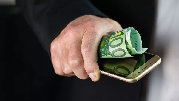 Una persona sostiene un movil y algunos billetes - Sputnik Mundo